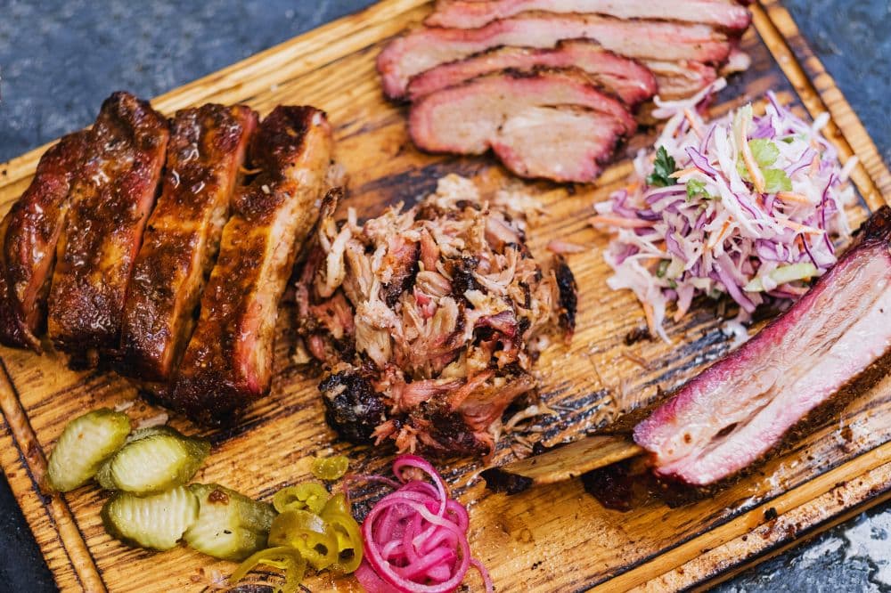 Sliced Pit Boss smoked brisket with a dark, crispy bark and juicy interior on a wooden cutting board, surrounded by salad and pickles.