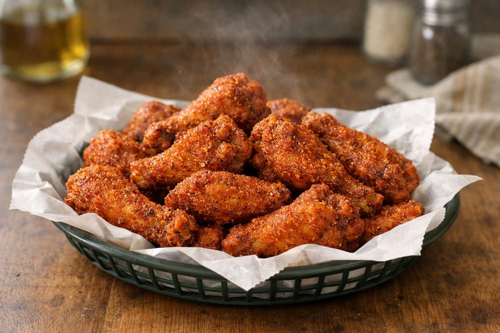 A paper-lined basket of crisp chicken wings coated in a dry orange-red hot honey rub