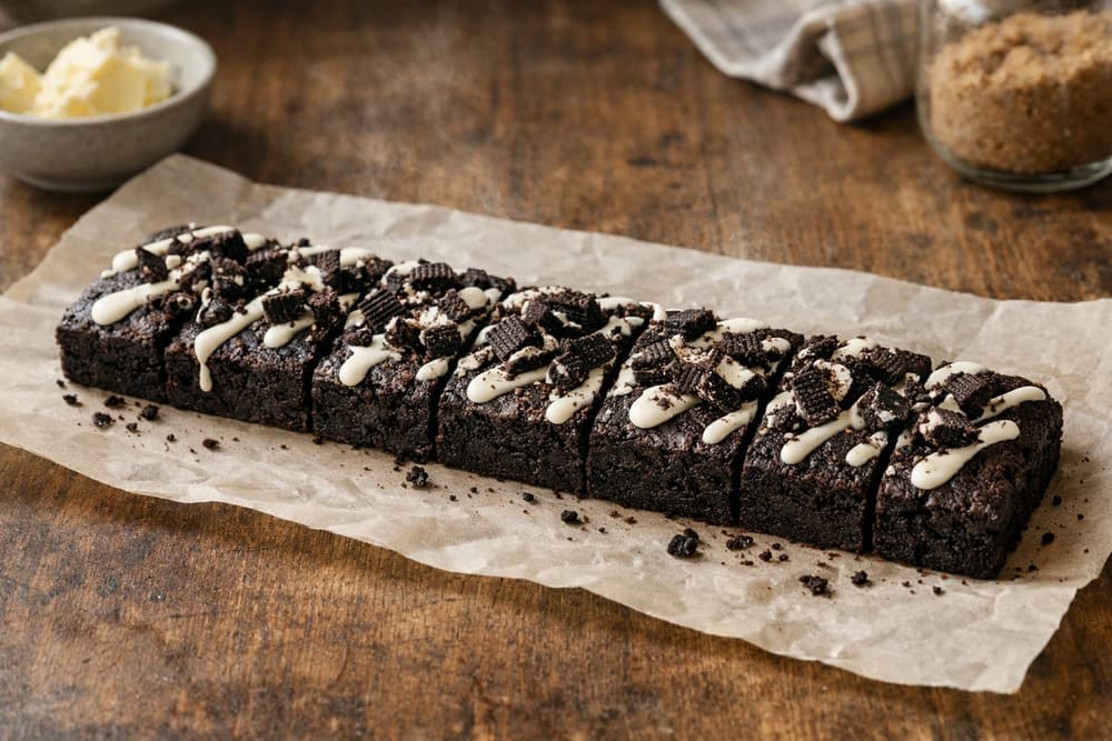A foot-long chocolate cookie bar with a vanilla cream drizzle and chopped chocolate sandwich cookies on top, cut in pieces